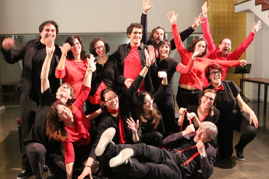 Foto de grup d'En Clau Vocal després del concert: els cantaires, de negre i vermell, posen amb els braços enlaire i alguns estirats a terra.