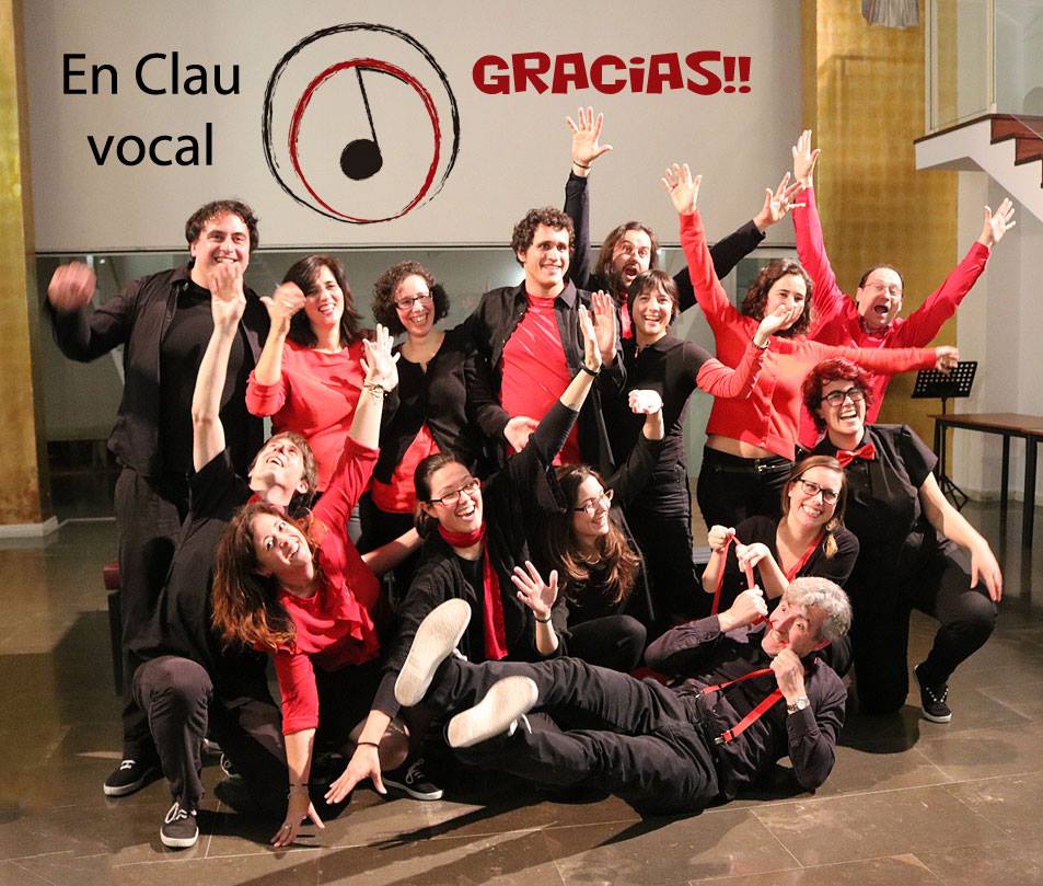 Foto de grup d'En Clau Vocal, de negre i vermell, amb els braços enlaire; a dalt hi ha el logotip del cor i el text «Gràcies!!».