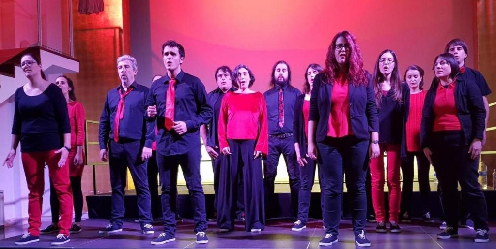Els cantaires d'En Clau Vocal, de negre i vermell, canten a l'escenari del Centre Cívic Pere Pruna sota una llum rosada.