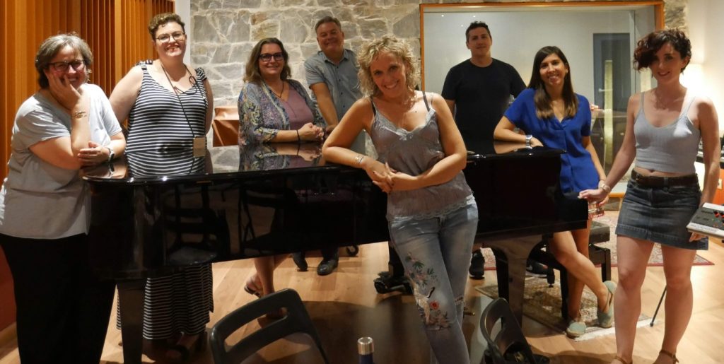 Foto de grup de l'Undercover Choir, recolzats en un piano de cua en una sala d'assaig.